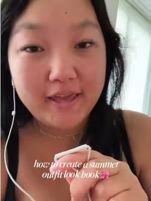 A close-up shot of a young woman with dark hair, wearing a black top and a delicate necklace, holding white wired earphones and a small white object, possibly a phone or remote. Text overlay states 'how to create a summer outfit look book'. She is looking directly at the camera, expressing and speaking. The background is soft, with glimpses of a light colored wall and a window to the right.
