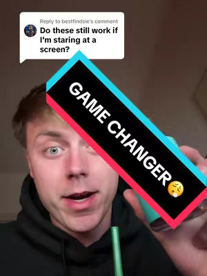 A young man with light skin is the central figure, positioned with his head and shoulders visible. He has short brown hair and is looking towards the camera with a slightly surprised expression. A text overlay in a rectangular format, diagonally across the image, reads
GAME CHANGER
in large, white letters on a black background, with a stripe of cyan and red on either side. The man is holding a teal-colored product, perhaps a bottle or a pen, at the forefront. The background is a neutral tone, possibly a wall. A speech bubble is in the top left corner. The image has an unfiltered, candid feel, typical of a selfie or a casual video.