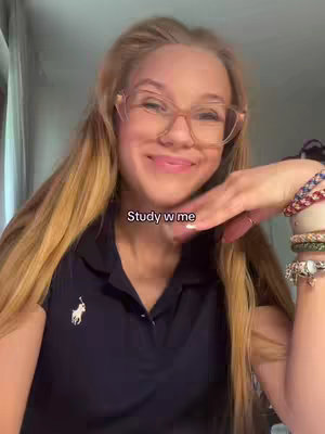 A young woman with long blonde hair and glasses smiles at the camera, resting her cheek on her hand. She wears a dark blue polo shirt. The text 'Study w me' is overlaid on the image.
