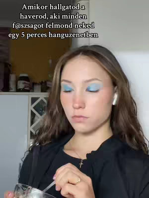 A young woman is shown in a medium shot, facing the camera with closed eyes. She has medium-length brown hair and is wearing blue eyeshadow, a black shirt, and an earring. The background shows blurry elements. The text overlay on the image is in the upper part of the image.