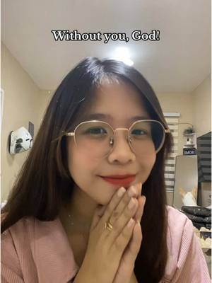 A selfie-style shot featuring a young woman with long, dark hair and glasses, looking directly at the camera with a gentle smile. She is in a cozy-looking indoor setting, likely her home, and holds her hands together in a prayer-like gesture. Above her head, text overlayed reads "Without you, God!"