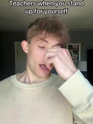 A young man with fair skin and light brown hair is shown from the chest up, in a selfie-style video. He is in a room with a beige wall and some natural light. The man is wearing a light-colored, long-sleeved shirt. He is touching his face and appears to be reacting to what he's saying. The overlay text is white and located at the top of the video.