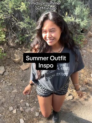 The cover image shows a woman smiling and facing the camera while in a natural setting. She is wearing a gray t-shirt, black and white shorts, and black boots. There is text overlayed on the image that says "Summer Outfit Inspo". The background includes greenery and dirt. The composition is a medium shot, which highlights her upper body against a natural backdrop.
