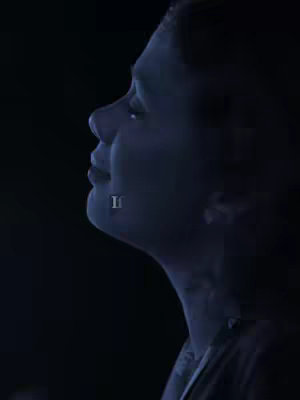 A side profile of a person's face, with the facial features softly illuminated against a dark backdrop, focusing on the nose, mouth, and jawline.