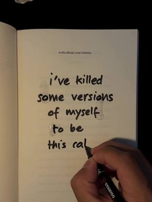 A hand writing on a open book. The text on the page says "write about your trauma," and there is also a handwritten text with the pen which states "i've killed some versions of myself to be this cal".