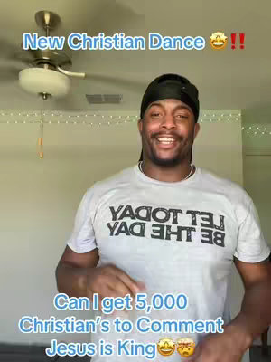 The image features a man standing indoors, smiling at the camera. The background is a neutral-toned wall with a ceiling fan and a string of decorative lights. Text overlays at the top and bottom of the frame announce the content: 'New Christian Dance' and 'Can I get 5,000 Christian's to Comment Jesus is King', respectively.