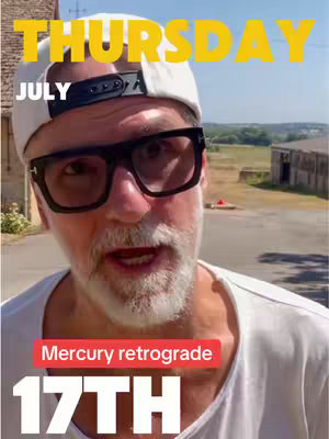 A front-facing selfie-style shot of a man wearing a white cap and oversized black-rimmed glasses, standing outside. The background features a slightly blurred view of a building and greenery under a bright, sunny sky. Text overlays in yellow and red indicate the day and date as 'THURSDAY JULY' and '17TH', along with 'Mercury retrograde'.