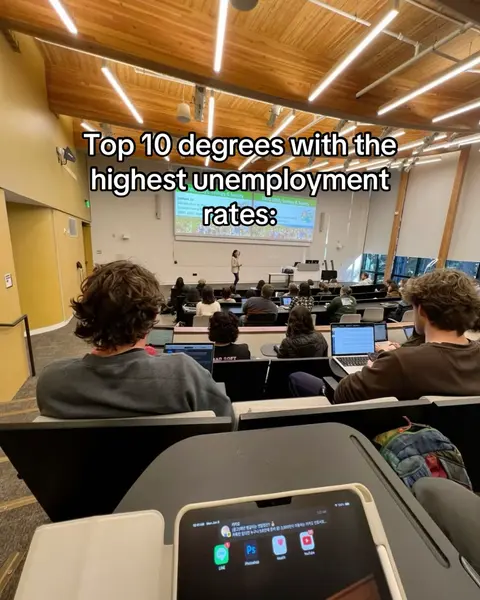 An image of a university lecture hall from the perspective of a student. The hall is filled with rows of students facing a screen displaying a presentation. Text overlays the top of the image. A phone is visible in the foreground on the student's desk.