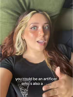 A woman with light skin and long, highlighted brown and blonde hair is centered in the frame, looking slightly surprised. She's lying down on a green surface, and her black t-shirt displays a graphic. Text overlays appear at the bottom of the frame in a white, sans-serif font.