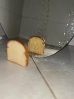 The cover image shows two slices of bread. One slice is on a white surface, appearing close to the viewer, while the other slice, also buttered, is reflected in a mirror or shiny surface. The composition is simple, focusing on the bread.