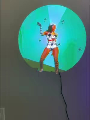 The image features a woman in a stage costume, standing on a platform in front of a turquoise circle.