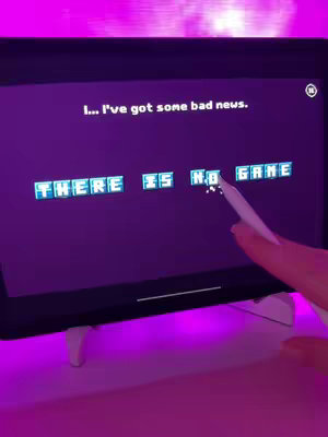 A handheld tablet displays the words 'THERE IS NO GAME' on a dark purple screen. A hand with a white stylus interacts with the screen, indicating gameplay, with a hint of pink light illuminating the surroundings.