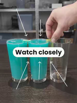 The image shows three tall glasses, two filled with a teal liquid and one empty, arranged on a dark surface. A hand holds a yellow strip, possibly to connect the glasses, with arrows pointing from the glasses and the liquid, and text overlay at the center.