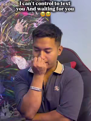 A young man is shown in a close-up shot, with a worried expression and hand covering his mouth. He's wearing a dark blue collared shirt, adorned with a light-colored bracelet. The background is a blend of abstract art and a gaming chair.