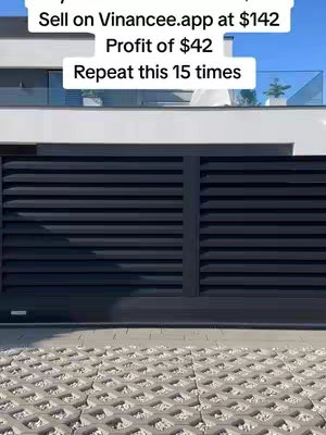 The image shows a modern-looking building with a black, slatted gate. Above the gate is a white rectangle with text in black, and a light blue sky is visible above with glass railing.
