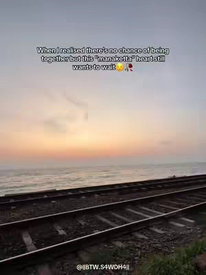 The image captures a serene coastal scene at dusk, featuring the convergence of the sea, sky, and railway tracks. The sky transitions across hues of orange and yellow, above a calm sea. In the foreground, railway tracks extend towards the horizon. Text overlayed on the image conveys a message about enduring feelings in a relationship.