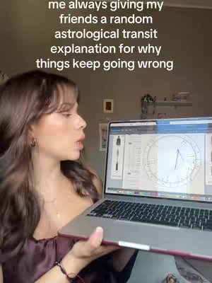 A woman with long brown hair holds a silver laptop, displaying an astrological chart. She's wearing a burgundy top, and the background is muted, suggesting an indoor setting. Text overlaid reads, 'me always giving my friends a random astrological transit explanation for why things keep going wrong.'
