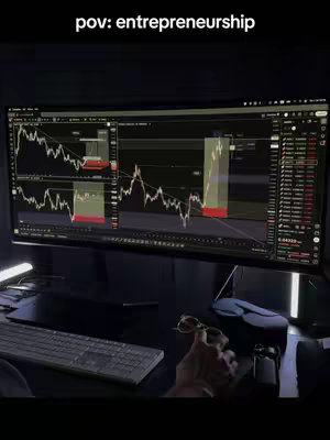 A perspective shot featuring a dark, modern workspace with a large computer monitor displaying financial charts and data. The lighting suggests a nighttime setting. The POV shot includes a desk, keyboard, and a hand in the foreground holding glasses, providing a context of someone working on financial analysis or trading.