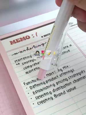 A hand holding a pen over a notebook with handwriting notes. The notes are about marketing with a pink color background.