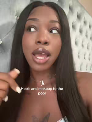 A woman with long black hair and full lips is looking upwards and slightly to the side with an open mouth, as if mid-sentence. She is wearing a necklace, and her right index finger is pointing downwards. overlaid text reads, 'Heels and makeup to the pool'.