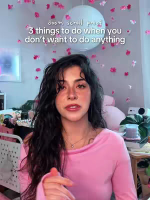 The cover image features a young woman centered in the frame, looking directly at the camera. She has dark, wavy hair. The backdrop is a soft, pink-themed room with decorations of pink flower petals. Text overlays at the top read, 'doom scroll proof' and '3 things to do when you don't want to do anything.'
