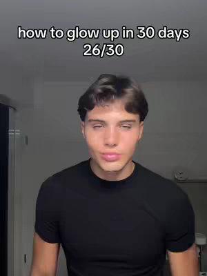 A young man is centered in the frame, with a dark, plain background behind him. He is wearing a black t-shirt. Above him is a text overlay written in a sans-serif font, which reads 'how to glow up in 30 days' followed by '26/30'. The man has short, dark hair. He has slightly closed, relaxed eyes. The lighting suggests an artificial light source.