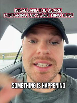 A man in a black cap is sitting in a car with text overlays. The background hints at a parking lot on an overcast day. The man, with a beard and slight smile, is looking directly at the camera. The text overlays, in a bold, white font, announce a potential escalation of the Israel-Iran conflict and a WW3 scenario. The overall composition is simple, focusing on the man's face and the layered text conveying a sense of urgency and speculation.