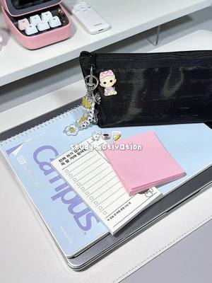 A flat lay of study materials on a desk, featuring a pink keyboard, a black pencil case with a charm, notebooks, sticky notes, and a pen.