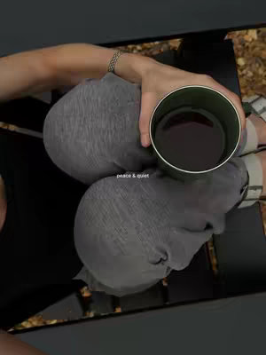 An overhead shot shows a person seated, with gray clothing.  Their head and an arm holding a cup of liquid are visible. The cup is round with a green exterior and a dark interior. The person's arm wears a silver bracelet.