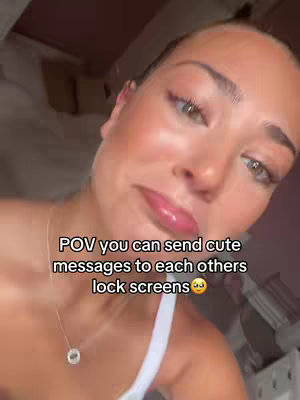 A close-up shot features a fair-skinned woman with highlighted features. Her expression is one of gentle affection, with slightly pursed lips and soft eyes. The lighting indicates a close-up selfie, positioned with the focus on her face, and the background is slightly blurred.