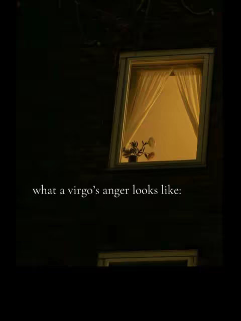 A dimly lit image showing a building exterior at night. In the center is a rectangular window with a warm, yellow light emanating from within. The window has white curtains and a glimpse of a plant inside. The text overlay reads "what a virgo's anger looks like:". The surroundings are dark, suggesting a nighttime scene.