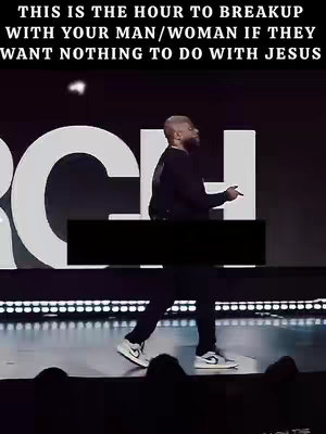 A man wearing a black outfit is walking down a dark stage with the text overlayed at the top. The man appears to be gesturing with his right hand and an area of the image is covered with black to obscure text. The stage has a large logo on the background.