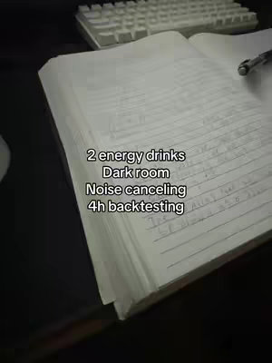A notebook with handwritten notes is open on a desk, with a keyboard visible in the background. Text overlays list, "2 energy drinks, Dark room, Noise canceling, 4h backtesting."