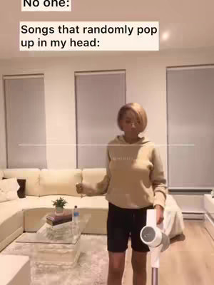 A woman in a beige hoodie and black shorts stands in a living room, holding a vacuum cleaner. Text overlays announce 'No one' and 'Songs that randomly pop up in my head:' in white boxes.