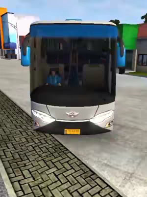 A front-facing view of a bus parked on a brick road. The bus is silver, with a blue roof. The camera is positioned at the bus's eye level, giving the viewer the perspective of standing in front of it. The background contains a blurry street and buildings.