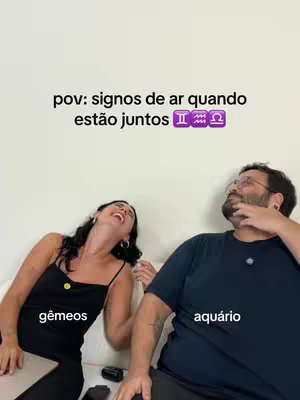 The image shows a selfie style shot featuring a woman laughing and a man looking up with a thoughtful expression, both sitting on a white couch. Text overlays indicate astrological signs: "gêmeos" (Gemini) near the woman and "aquário" (Aquarius) near the man, with more text "pov: signos de ar quando estão juntos".