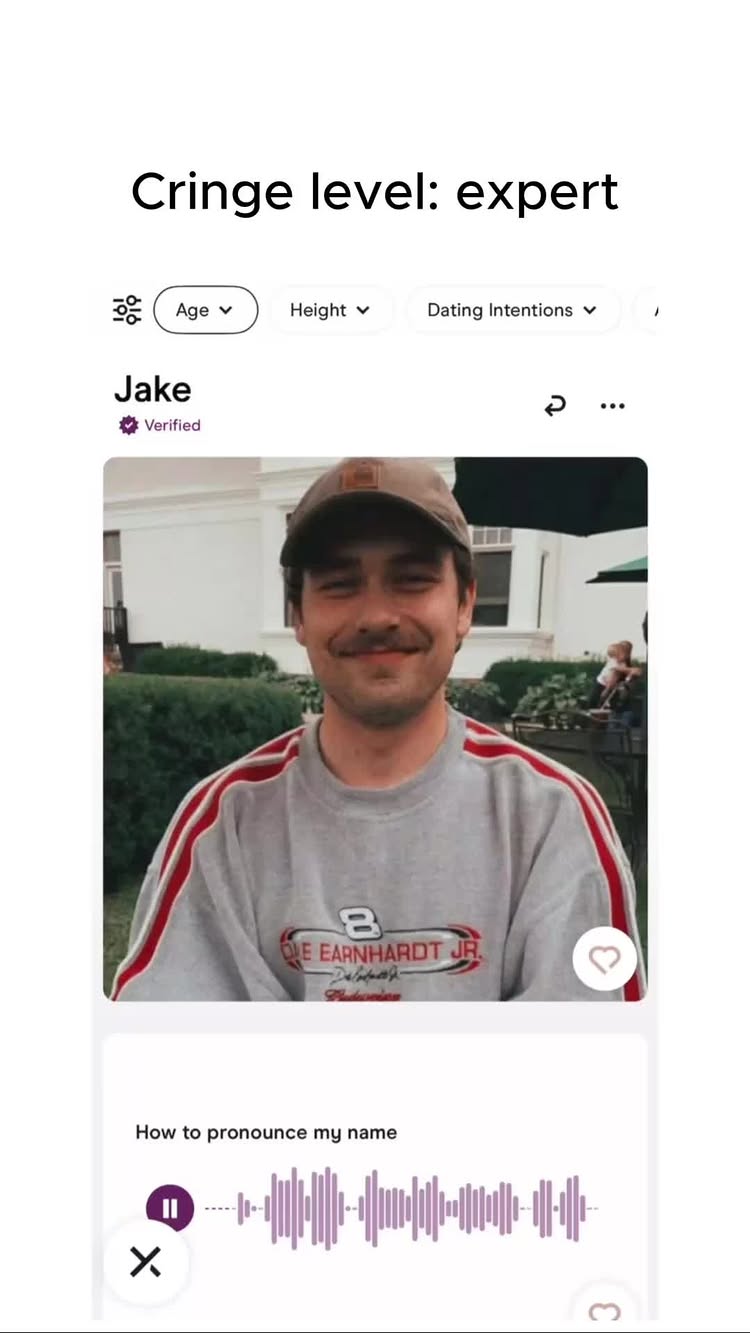 The image is a screenshot of a dating app profile. A man in a grey sweatshirt and a baseball cap is the focal point. His name, "Jake" with a verification check, is visible.  Additional text includes profile options like "Age," "Height," and "Dating Intentions."
