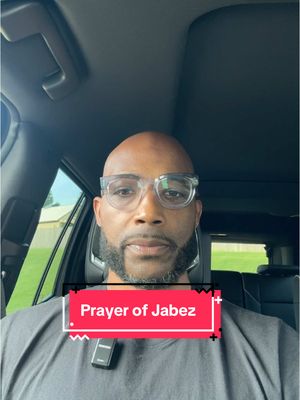 A man with a shaved head, clear-framed glasses, and a trimmed beard is seen from the chest up, seated inside a car. A text overlay with the words 'Prayer of Jabez' is prominently displayed on a red background in front of him. The background looks like the interior of a car. He appears to be looking directly at the camera.