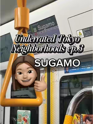 The cover image appears to be taken inside a train or subway car. In the foreground, there’s a yellow handgrip, and an animated emoji of a person giving a thumbs-up. Behind this is the train window or wall, where the text "Sugamo" is prominent. The background is slightly blurred with what looks like advertisements, the Sugamo train station sign, and other elements. A clear shot of the face emoji gives a clear focus