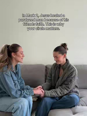 Two women are seated on a gray couch, facing each other, holding hands and looking at each other. The woman on the left wears a denim jacket and the woman on the right has a green jacket. Text is overlaid at the top of the image.