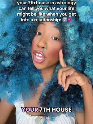 A selfie of a person with blue curly hair and light skin, wearing a white top. She is pointing with her right index finger and has blush on her cheeks. Text overlays describe astrology concepts and direct attention towards the topic.