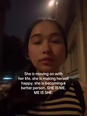 A selfie-style shot of a woman facing the camera. She's in what appears to be a nighttime setting with a streetlamp behind her. Overlayed text in white is positioned below her face, and she is shown wearing a black and white striped top.