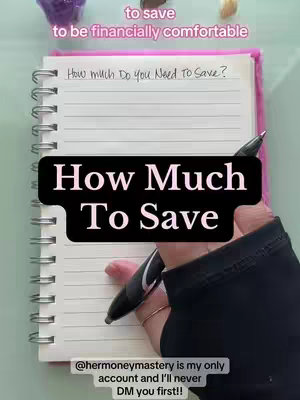The image is a close-up shot of a hand writing on a notepad. The notepad is open to a blank page, and a black pen is in the hand. Above is a text overlay that says 'to save' and 'to be financially comfortable'. The notepad and hand dominates the frame, with a small section of a pink cover visible and some crystals. The image uses a natural color palette, with the primary colors being white, black, pink, and green.