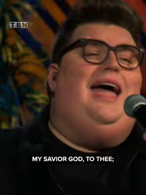The cover image is a medium shot of a man with glasses singing into a microphone. The background is unclear, but appears to have colorful, abstract patterns. The color palette is warm, with a focus on the man's skin tone and dark glasses frame.