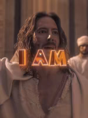 The image shows a man, assumed to be Jesus, with long brown hair and a beard, looking upwards with an open mouth. Overlaid on the image is the text 'I AM' in a glowing, golden font. The background is blurred, suggesting a crowd or a building.