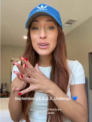 A woman wearing a blue cap and a white shirt is facing the camera and talking. The text "September J.E.S.U.S. challenge" is overlaid on the image with a blue heart emoji. The caption states the challenge is to put God first.