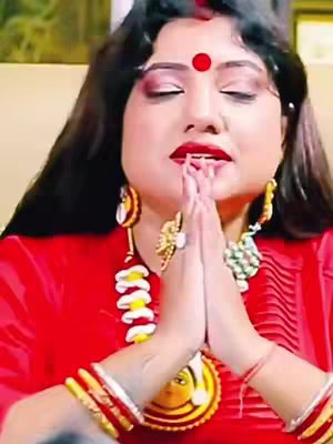 A woman with closed eyes and hands clasped in prayer. She wears a red bindi, red lipstick, and elaborate jewelry. The background is a diffused light.