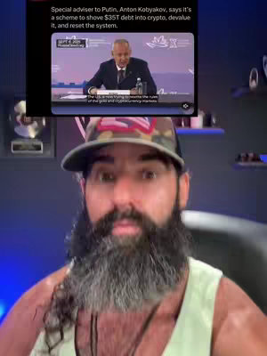 A man with a long beard is in the foreground, looking directly at the camera with a surprised expression. Behind him, a screen displays an image of a man in a suit speaking, with text overlaying the image. The overall composition is a selfie-style video.