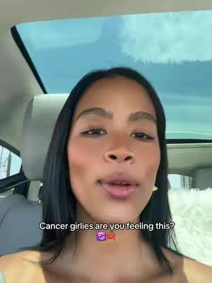 A selfie-style video with the creator in the front seat of a car. She has dark hair and is looking at the camera. The background shows a view of the sky through a car's sunroof.