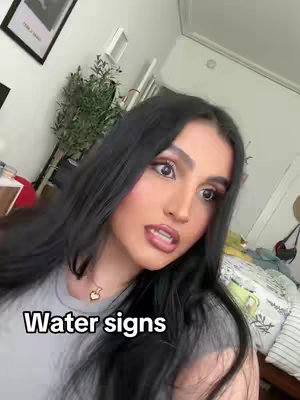 A woman with long black hair looks directly at the camera with a slight smile. Text overlay 'Water signs' is placed at the bottom. The background includes parts of a room.